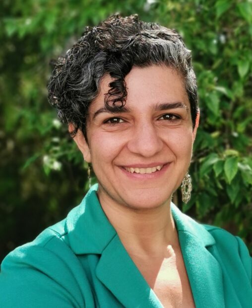 aftab erfan photo - short curly black hair, green blazer, standing in the sunshine